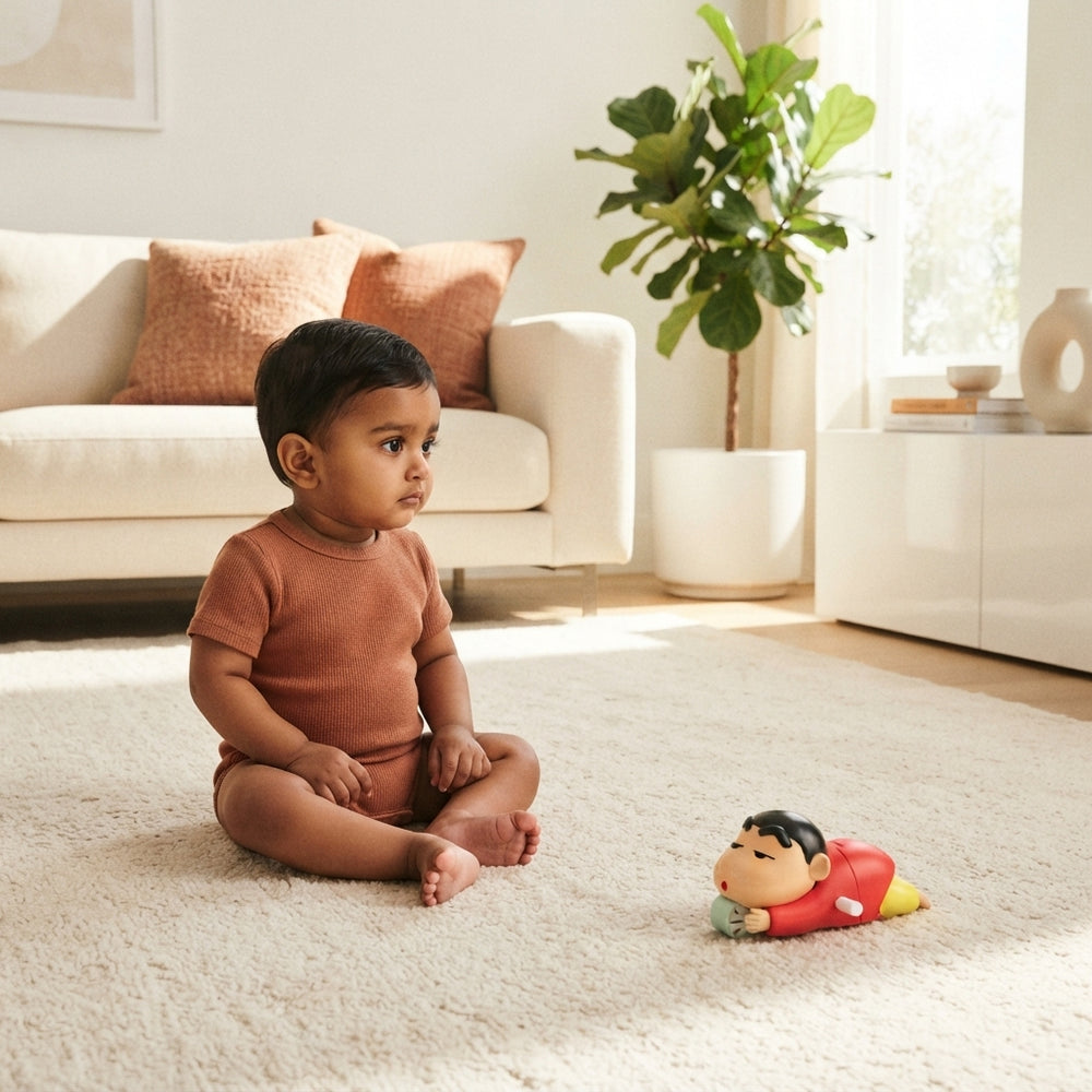 A South Asian baby sitting still on a cream rug next to a Shinchan toy in a modern, terracotta-accented living room.